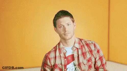 A Man In A Plaid Shirt Is Giving Two Thumbs Up In Front Of An Orange Wall . GIF