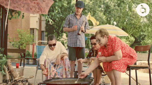 A Man In A Plaid Shirt Is Holding A Bottle Of Beer While A Group Of People Sit Around A Pan GIF
