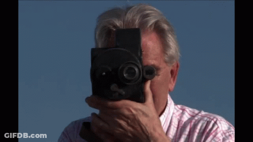 A Man In A Plaid Shirt Is Holding A Camera GIF