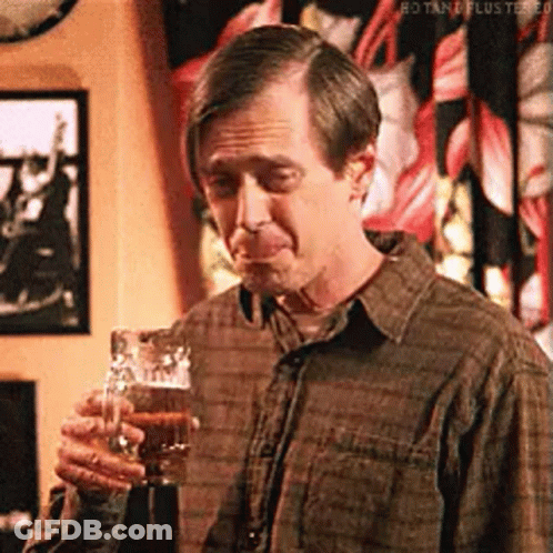 A Man In A Plaid Shirt Is Holding A Glass Of Beer And Making A Funny Face . GIF