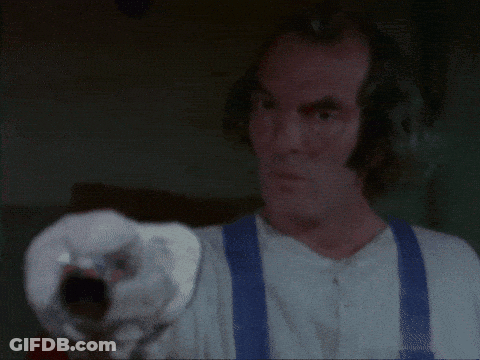 A Man In A Plaid Shirt Is Holding A Gun In His Hand . GIF