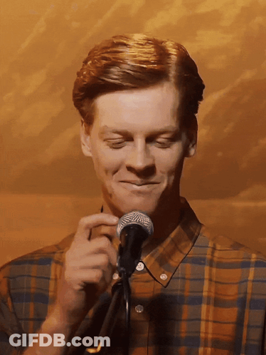 A Man In A Plaid Shirt Is Holding A Microphone And Smiling GIF