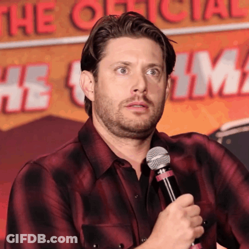 A Man In A Plaid Shirt Is Holding A Microphone In Front Of A Sign That Says " The Official " GIF