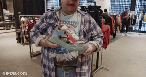 A Man In A Plaid Shirt Is Holding A Pair Of Shoes In His Hands GIF