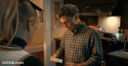 A Man In A Plaid Shirt Is Holding An Apple Product In His Hand GIF