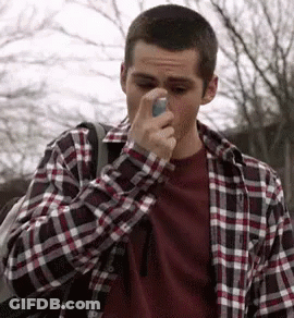 A Man In A Plaid Shirt Is Holding An Asthma Inhaler To His Nose . GIF
