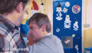 A Man In A Plaid Shirt Is Holding Another Man In His Arms In Front Of A Blue Wall With Snowmen On It . GIF