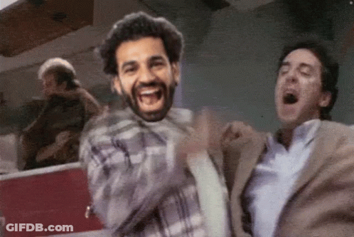 A Man In A Plaid Shirt Is Laughing While Another Man In A Suit Is Yawning . GIF