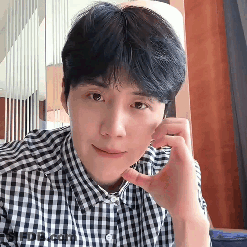 A Man In A Plaid Shirt Is Looking At The Camera With His Hand On His Face GIF