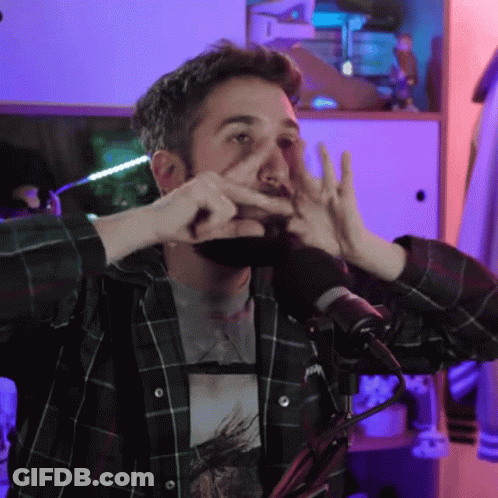 A Man In A Plaid Shirt Is Making A Face With His Hands In Front Of A Microphone GIF