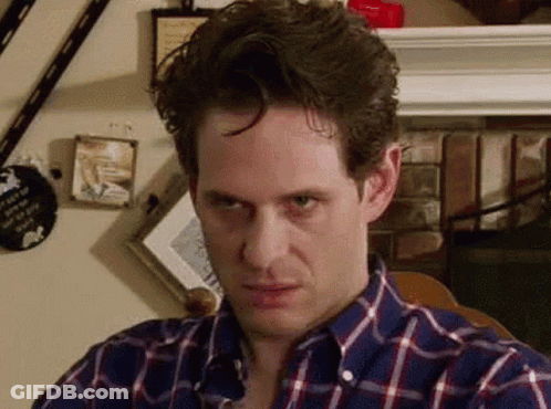 A Man In A Plaid Shirt Is Making A Funny Face And Looking At The Camera . GIF
