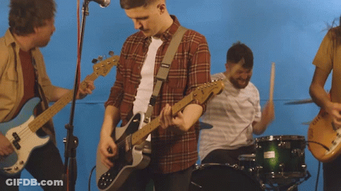 A Man In A Plaid Shirt Is Playing A Guitar In Front Of A Drum Set GIF