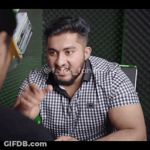 A Man In A Plaid Shirt Is Pointing At Another Man In A Black Shirt GIF