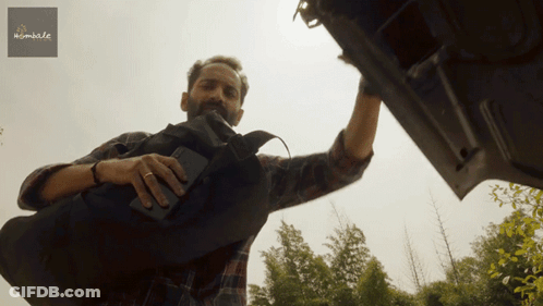 A Man In A Plaid Shirt Is Reaching Into The Trunk Of A Car With A Sign Above Him That Says Mumble GIF
