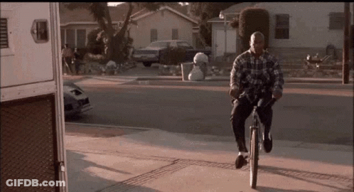 A Man In A Plaid Shirt Is Riding A Bike Down The Street GIF