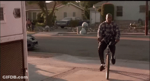 A Man In A Plaid Shirt Is Riding A Bike On A Sidewalk GIF
