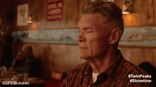 A Man In A Plaid Shirt Is Sitting At A Table With His Eyes Closed In A Diner . GIF