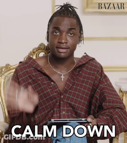 A Man In A Plaid Shirt Is Sitting In A Chair And Holding A Tablet With The Words Calm Down Written On It GIF
