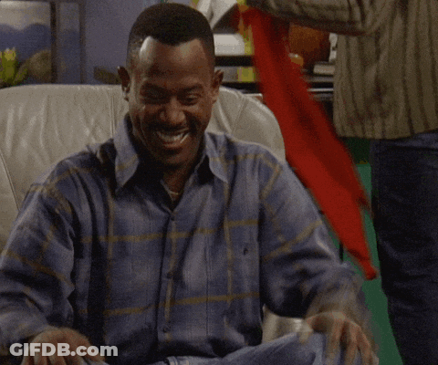 A Man In A Plaid Shirt Is Sitting In A Chair And Laughing GIF