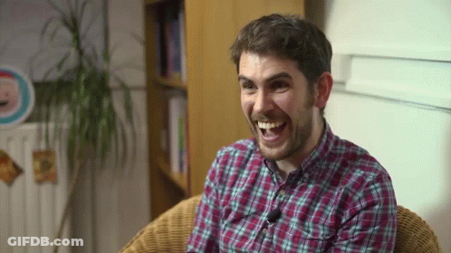 A Man In A Plaid Shirt Is Sitting In A Chair And Smiling GIF