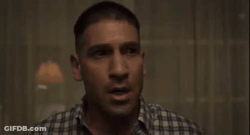 A Man In A Plaid Shirt Is Sitting In A Dark Room GIF