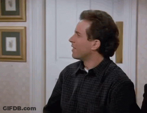 A Man In A Plaid Shirt Is Sitting In A Room With A Door . GIF