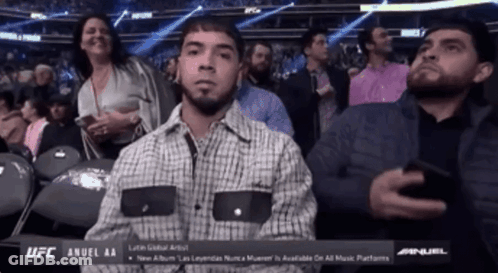 A Man In A Plaid Shirt Is Sitting In A Ufc Stadium GIF