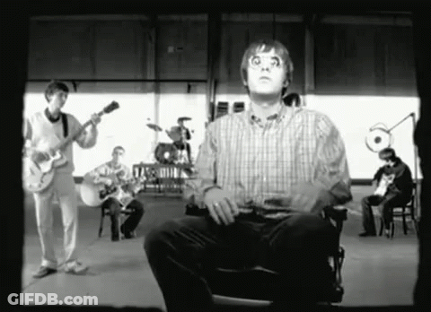 A Man In A Plaid Shirt Is Sitting In Front Of A Group Of Musicians GIF