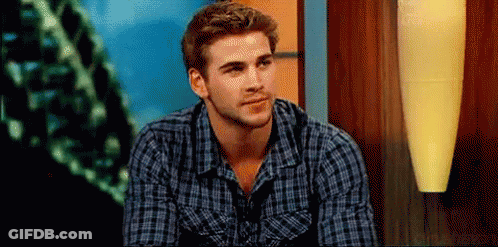 A Man In A Plaid Shirt Is Sitting In Front Of A Lamp And Looking At The Camera . GIF