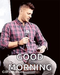 A Man In A Plaid Shirt Is Sitting In Front Of A Microphone And Holding A Glass Of Wine . GIF