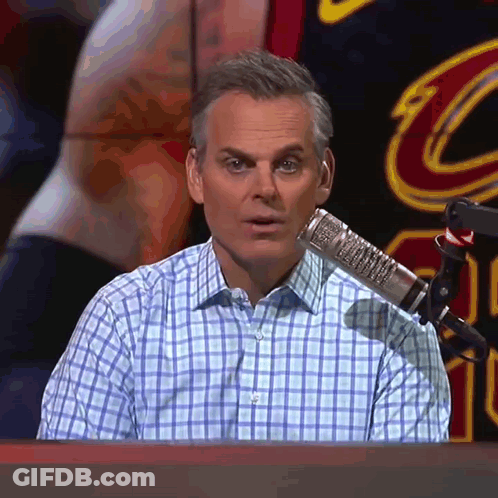 A Man In A Plaid Shirt Is Sitting In Front Of A Microphone In Front Of A Cleveland Cavaliers Logo GIF