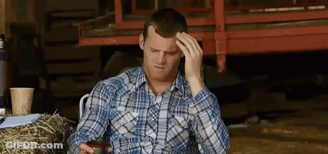 A Man In A Plaid Shirt Is Sitting In Front Of A Pile Of Hay And Holding His Head . GIF