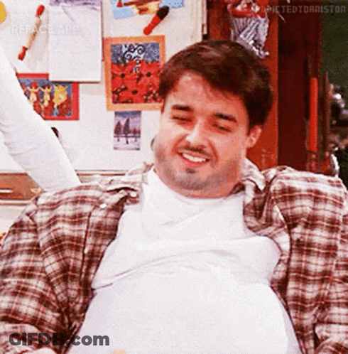 A Man In A Plaid Shirt Is Sitting In Front Of A Refrigerator With His Eyes Closed . GIF
