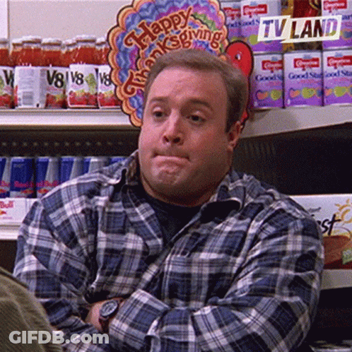 A Man In A Plaid Shirt Is Sitting In Front Of A Sign That Says Happy Thanksgiving On It . GIF