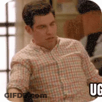 A Man In A Plaid Shirt Is Sitting In Front Of A Window And A Sign That Says Uc . GIF