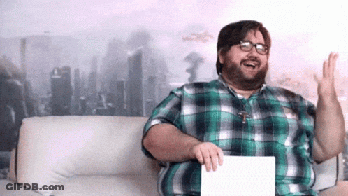 A Man In A Plaid Shirt Is Sitting On A Couch And Holding A Piece Of Paper GIF