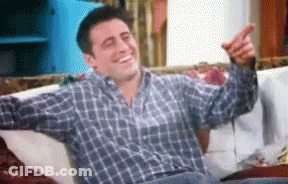 A Man In A Plaid Shirt Is Sitting On A Couch Pointing GIF
