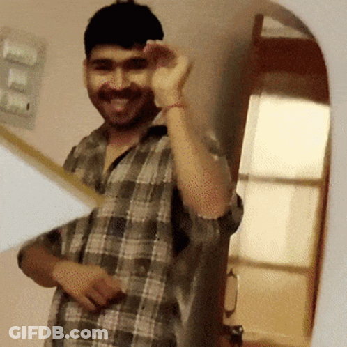 A Man In A Plaid Shirt Is Smiling And Waving At The Camera GIF