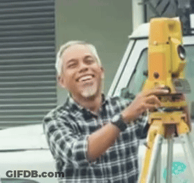 A Man In A Plaid Shirt Is Smiling While Holding A Yellow Device On A Tripod GIF