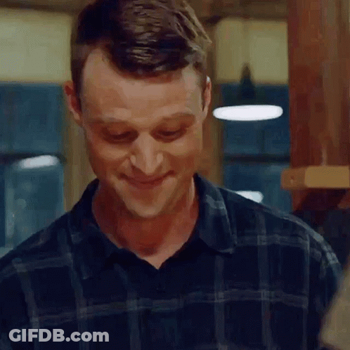 A Man In A Plaid Shirt Is Smiling While Standing In A Kitchen . GIF