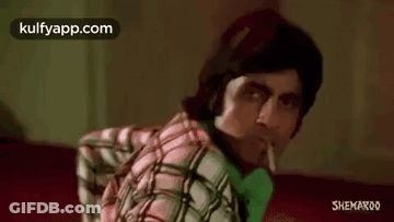 A Man In A Plaid Shirt Is Smoking A Cigarette While Sitting On A Red Couch . GIF