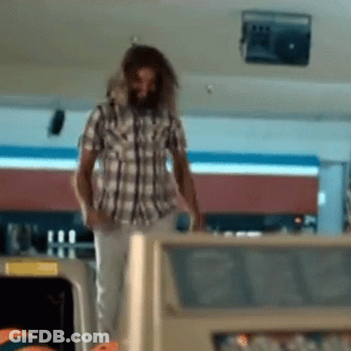 A Man In A Plaid Shirt Is Standing In A Bowling Alley Looking At A Bowling Ball GIF