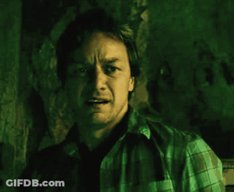 A Man In A Plaid Shirt Is Standing In A Dark Room GIF