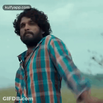 A Man In A Plaid Shirt Is Standing In A Field With His Arms Outstretched . GIF