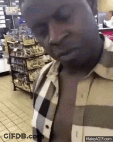 A Man In A Plaid Shirt Is Standing In A Grocery Store Looking Down . GIF