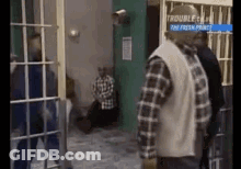A Man In A Plaid Shirt Is Standing In A Jail Cell With Other Men . GIF