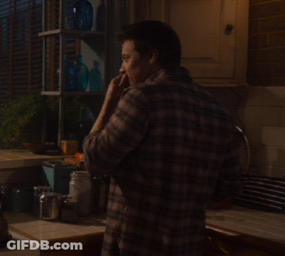 A Man In A Plaid Shirt Is Standing In A Kitchen Talking On A Cell Phone GIF