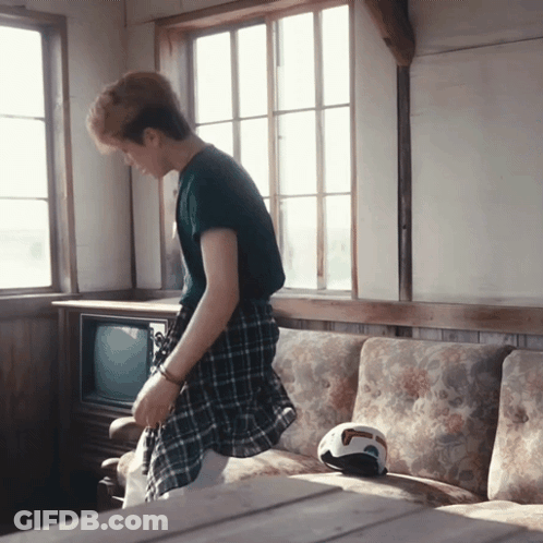 A Man In A Plaid Shirt Is Standing In Front Of A Couch GIF