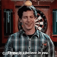 A Man In A Plaid Shirt Is Standing In Front Of A Dart Board . GIF