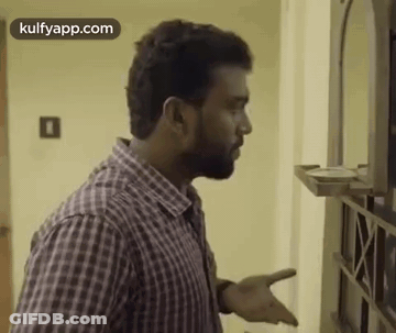 A Man In A Plaid Shirt Is Standing In Front Of A Mirror And Talking To Someone . GIF